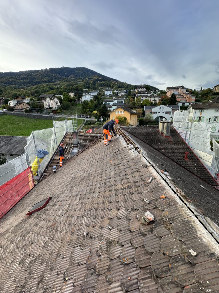 Démolition manuelle : ouvrier sur une toiture en cours de démontage à Monthey