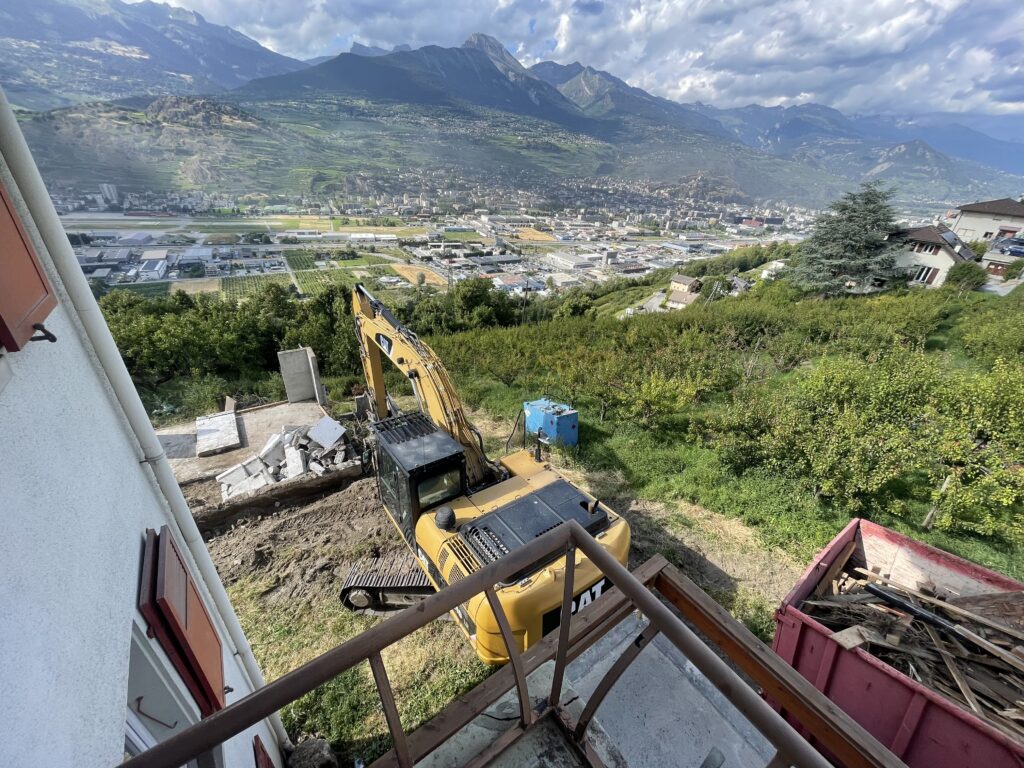 Mini-pelle sur un terrain en pente avec vue sur une vallée et des montagnes